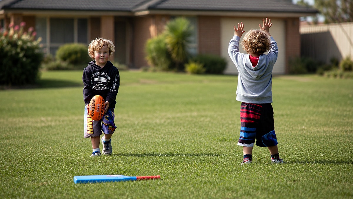 Two young Australian children playing on a suburban lawn with a football and plastic cricket bat outside a family home.